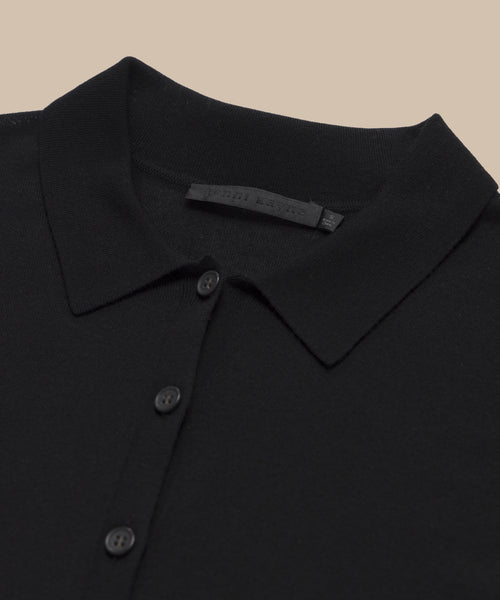 Close-up of the black Grayson Pullover, a casual polo sweater with a button-down front (three visible buttons) and an inner collar fabric tag, laid flat on a beige background.