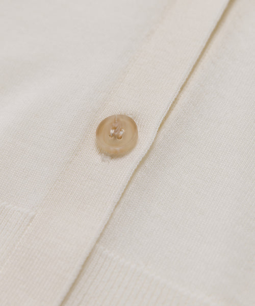 Close-up of the Mira Cardigan in ivory, showcasing a single round translucent button fastened through its knitted fabric.