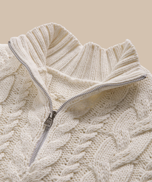 A close-up of the Cotton Cable Half Zip sweater, featuring its ivory cable-knit pattern and half-zip collar in lightweight cotton against a neutral background.