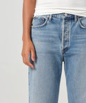 Wearing light blue Fran Jean high-waisted relaxed leg jeans with an untacked folded cuff and a white ribbed tank top, shown waist to mid-thigh with one hand at their side.