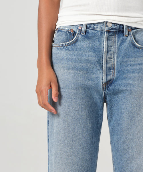 Wearing light blue Fran Jean high-waisted relaxed leg jeans with an untacked folded cuff and a white ribbed tank top, shown waist to mid-thigh with one hand at their side.