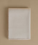 A folded cream-colored wool blanket with a soft, brushed texture and fringed edges, displayed on a solid beige background.