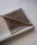 A folded blanket in warm taupe-brown shade set against a neutral light gray background.