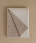 A folded wool blanket in a warm taupe-beige color, shown on a matching solid beige background.
