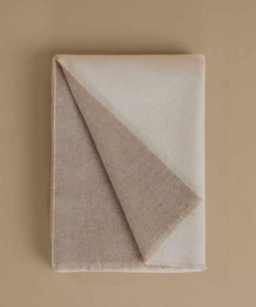 A folded wool blanket in a warm taupe-beige color, shown on a matching solid beige background.