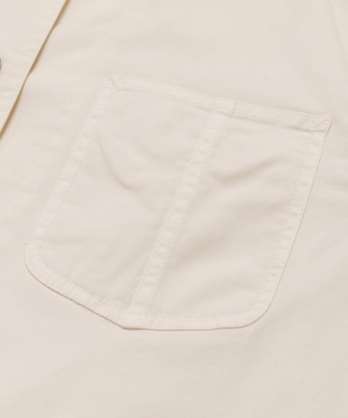 Close-up of the Gibson Jacket, a light beige summer-weight garment dyed canvas jacket with a stitched rectangular pocket, visible seam lines, and a smooth texture.