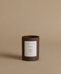 A glass candle with the scent Amber against a beige background.