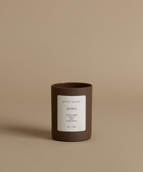 A glass candle with the scent Amber against a beige background.