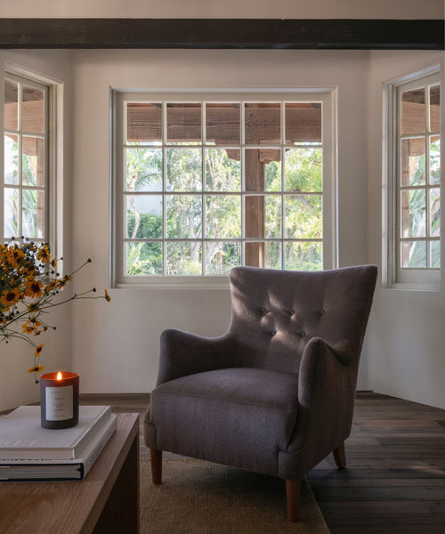 A living room with an accent chair, wood coffee table and a lit candle. 