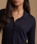 A close-up of a woman wearing a dark navy long-sleeve polo shirt against a warm beige background.