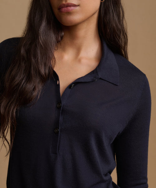 A close-up of a woman wearing a dark navy long-sleeve polo shirt against a warm beige background.