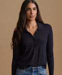A woman modeling a dark navy long-sleeve polo shirt with a buttoned collar, paired with blue jeans, against a solid warm beige background.