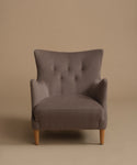 A single upholstered armchair with a high tufted back, curved arms, and light wood legs, shown against a plain warm beige studio background.