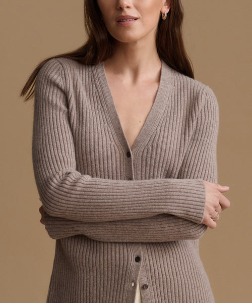 A woman wearing a ribbed knit cardigan sweater in taupe brown, shown from the chest up against a solid warm beige background.