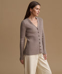 A woman wearing a ribbed knit button-front cardigan in taupe and cream wide-leg trousers, photographed against a solid warm beige studio background.
