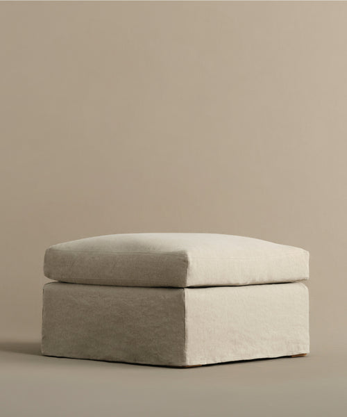 The Harbor Ottoman, a square piece in light beige with a cushion top, rests on a matching background for a minimalist, neutral-toned scene—capturing the signature style of Jenni Kayne Furniture.