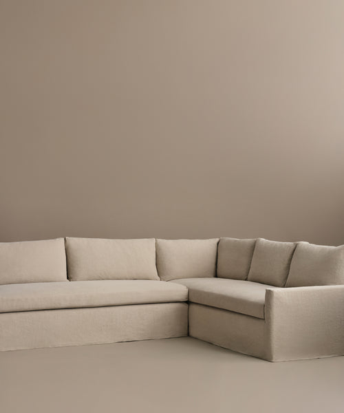 The Harbor Sectional, featuring clean lines and plush cushions in beige, sits against a matching beige wall and floor in a minimalist room.