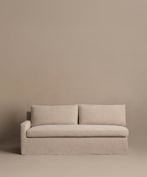 The Harbor Sectional is a minimalist Belgian flax linen sofa with two cushions and a left armrest, shown against a matching beige backdrop. Part of the Jenni Kayne Furniture collection.