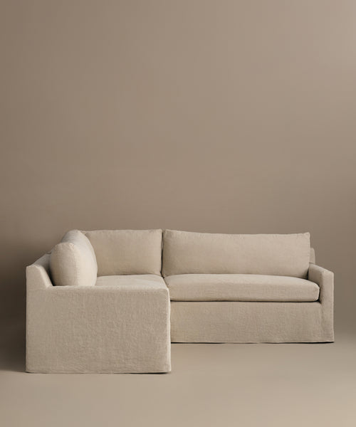 The Harbor Sectional features a minimalist design with clean lines and simple cushions, showcased in Belgian flax linen against a matching beige background.