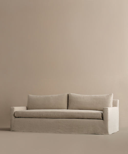 The Harbor Sofa, handmade in Los Angeles, showcases clean lines and two large seat cushions with linen upholstery for a modern look, set against a matching beige background.