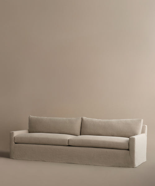 The Harbor Sofa features modern minimalist design with linen upholstery, two seat and back cushions, and a plain light brown background. Handmade in Los Angeles for timeless appeal.