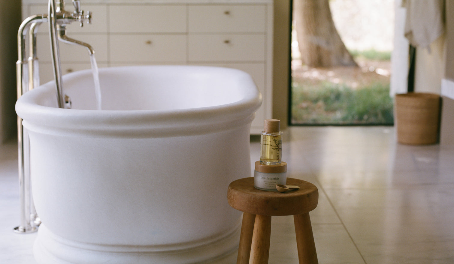 White freestanding bathtub with a wooden stool and bottle of shampoo in a bathroom setting.