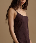 A woman wearing a dark brown satin slip dress with a subtle tonal damask pattern, shown in a close-up profile against a solid beige background.