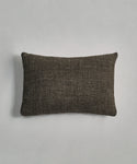 The Luna Lumbar Pillow, a rectangular dark brown handwoven pillow, is placed on a light gray surface.