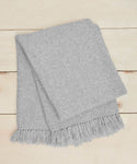 The Alpaca Basketweave Throw Rewards GWP, in light grey with fringed edges, is elegantly folded and displayed on a light wooden surface.