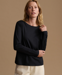 A woman modeling a black long-sleeve crewneck top with cream pants, set against a solid warm beige studio background.