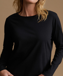 A close-up of a woman wearing a plain black long-sleeve crewneck top against a warm beige studio background.