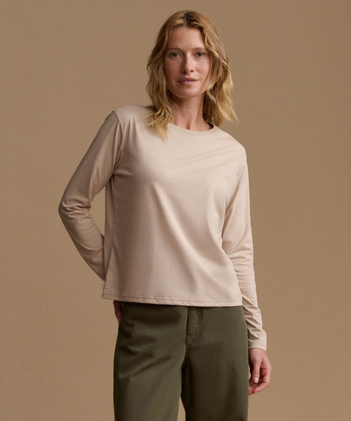 A woman modeling a light beige long-sleeve crewneck top with olive green pants, standing against a solid warm beige studio background.