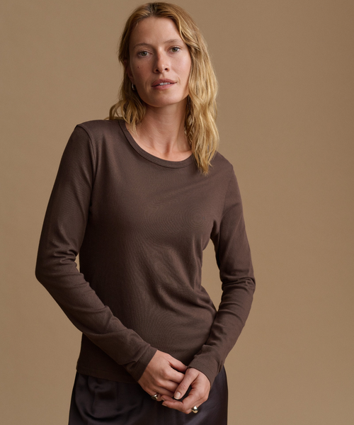 A woman modeling a dark brown long-sleeve crewneck top against a solid warm beige studio background.