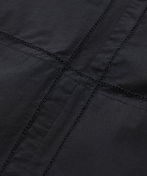 Close-up of the Lauren Skirt, highlighting its black cotton fabric and intersecting seam stitching that forms a cross pattern. The detailed texture and threads are clearly visible.