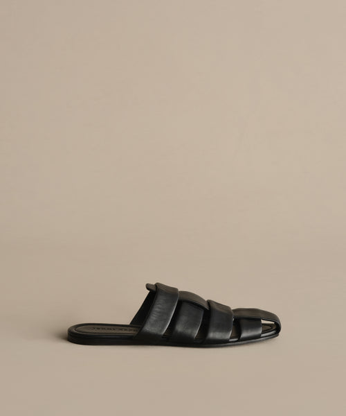 The Leather Camilla Mule is a black leather sandal featuring wide, padded straps and an open toe, shown on a neutral beige background.