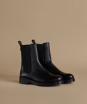 A pair of black leather Chelsea boots with elastic side panels, shown on a solid beige studio background.
