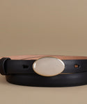 A black leather belt with a large, smooth, oval cream-colored buckle, photographed against a solid beige background.