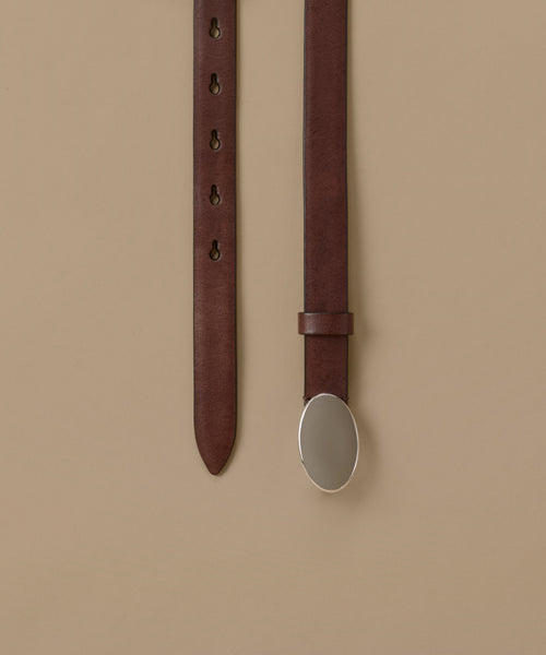 A dark brown leather belt with an oval silver-toned metal buckle, shown hanging vertically against a solid beige background.