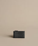 A compact black textured Leather Card Holder featuring three card slots and a zippered compartment, displayed on a plain beige surface with a minimalistic background.