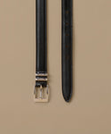 A black textured leather belt with a polished silver-tone buckle, shown laid flat against a solid beige background.