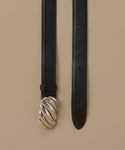 A black leather belt with a distinctive twisted silver-tone metal buckle, displayed vertically against a solid beige background.