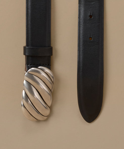 A close-up of a black leather belt with a distinctive silver-tone twisted rope buckle, shown against a solid beige background.