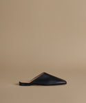 A single black leather mule slipper with a pointed toe and flat sole, shown in profile against a solid beige background.