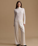 A woman modeling a cream-colored knit turtleneck sweater and matching wide-leg trousers against a solid beige studio background.