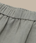 Close-up of a light gray, gathered waistband on the Linen Logan Short, showcasing visible stitching and gentle pleats for easy warm-weather style against a plain beige background.