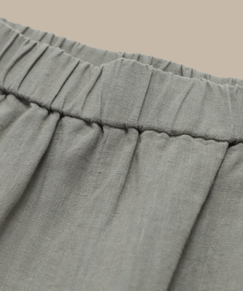 Close-up of a light gray, gathered waistband on the Linen Logan Short, showcasing visible stitching and gentle pleats for easy warm-weather style against a plain beige background.