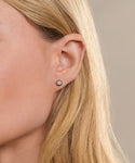 Close-up of a persons ear with straight blonde hair, wearing Liv Rose Cut Studs—small, round earrings featuring rose cut diamonds set in gold. The background is neutral and softly blurred.