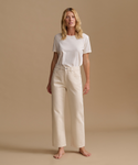 A model wearing a white t-shirt with cream color jeans in a studio.