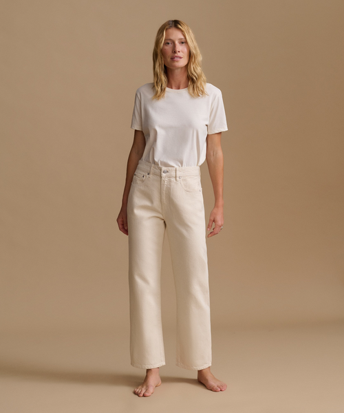 A model wearing a white t-shirt with cream color jeans in a studio.