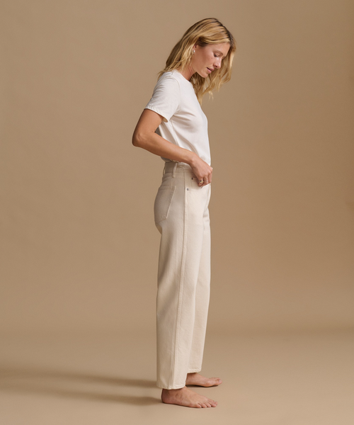 A model wearing a white t-shirt with cream color jeans in a studio.